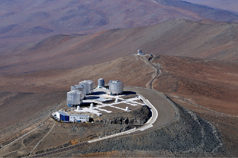 Photograph of four telescope buildings of the European Southern Observatory’s Very Large Telescope array, taken at night. In the distance, the building holding VISTA is visible.