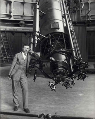 Photograph of Edward Emerson Barnard leaning against a large telescope.