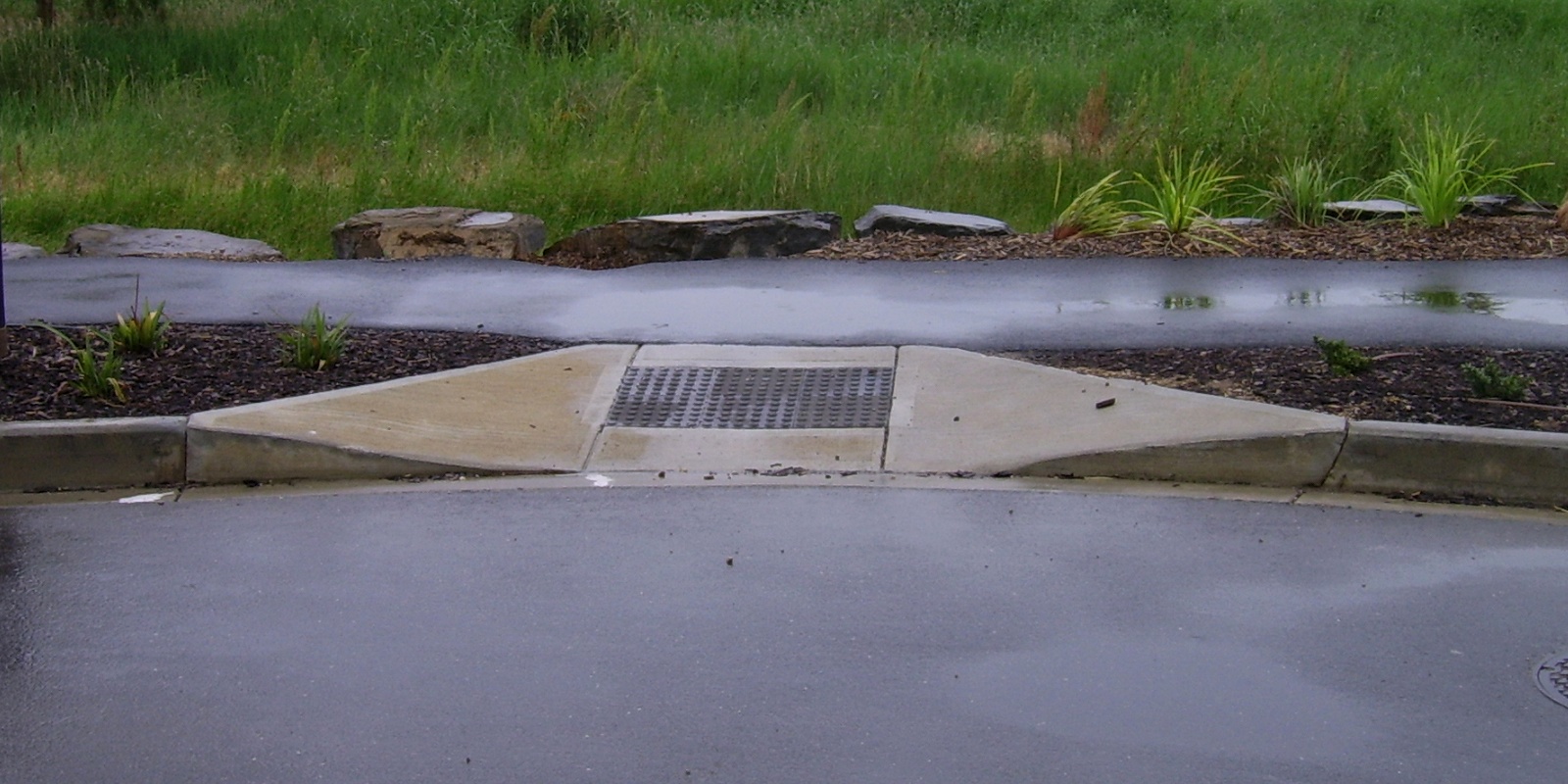A curb cut in a sidewalk on a rainy day