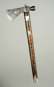 Photo of pipe tomahawk, 1790-1820. Iron tomahawk head with pipe bowl projecting from back; circular silver inlay with shield-breasted eagle incised on one side of blade, and heart-shaped silver inlay on the other.