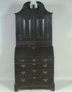 Black painted maple Queen Anne desk and bookcase; upper part has scrolled, broken pediment and two panel doors above two drawers; lower part is slant top desk with four graduated drawers; lid opens to reveal row of ten pigeon holes above row of five drawers; shaped skirt and bracket feet; brass bail handles on brass escutcheons (not original).