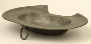 Oval pewter shaving basin with double-reeded brim; oval ring attached beneath rim.