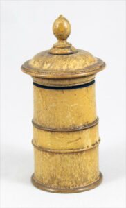 Wood inkstand composed of turned cylindrical body which can be unthreaded to reveal lower sand compartment; upper compartment is fitted with glass inkwell; threaded lid has urn-shaped finial; inkstand is covered in yellow varnish.