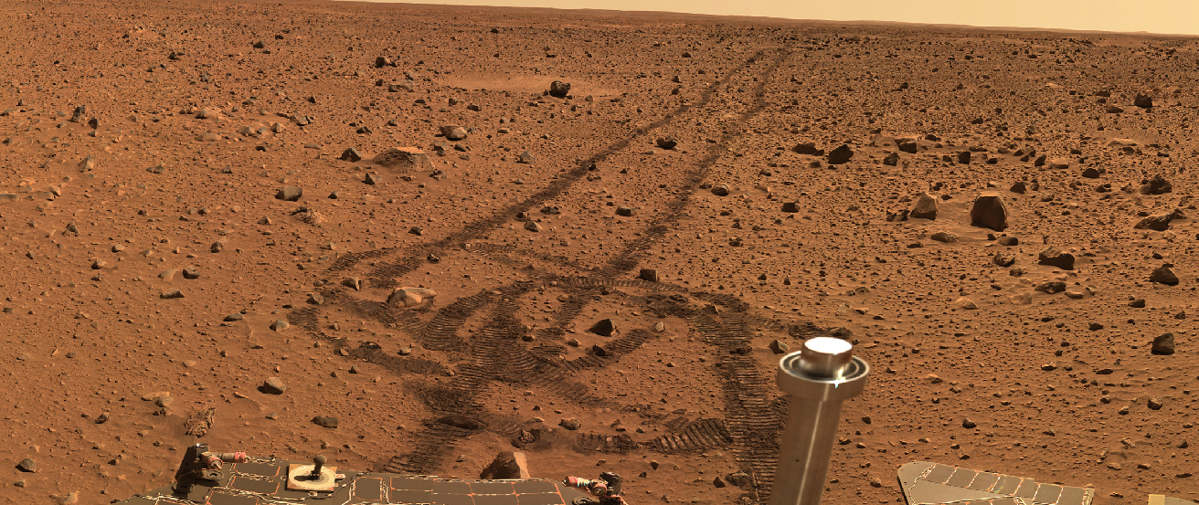 Spirit Rover on Mars. Beginning in the upper right of this photograph, the tracks left by the passage of the Spirit rover are visible on the flat, rock strewn martian terrain. At the bottom, the tracks form a loop where the rover changed direction, and portions of the rover’s body are seen.