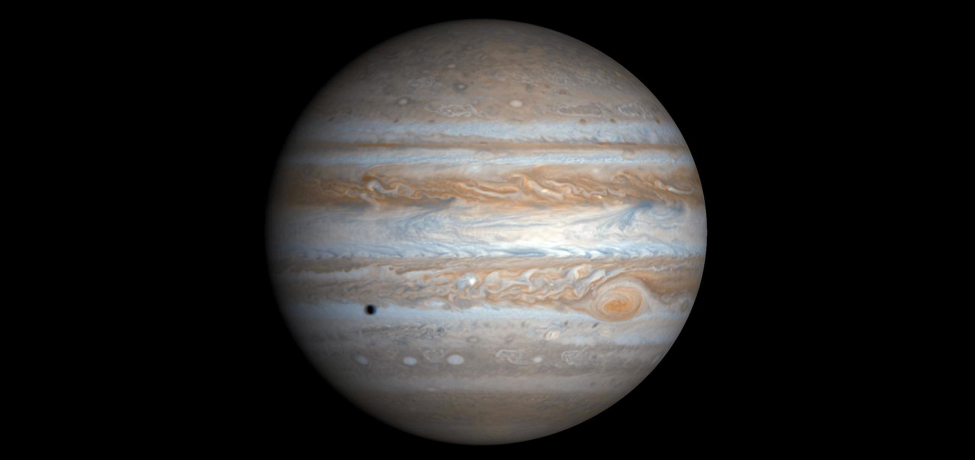 Photograph of Jupiter. Taken from the Cassini spacecraft, the alternating light and dark cloud bands are visible over the entire planet. The Great Red Spot is at lower right. Also seen is the shadow of the moon Europa at lower left.