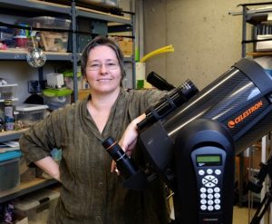 Woman standing in front of an 8 inch telescope, smiling at the camera.