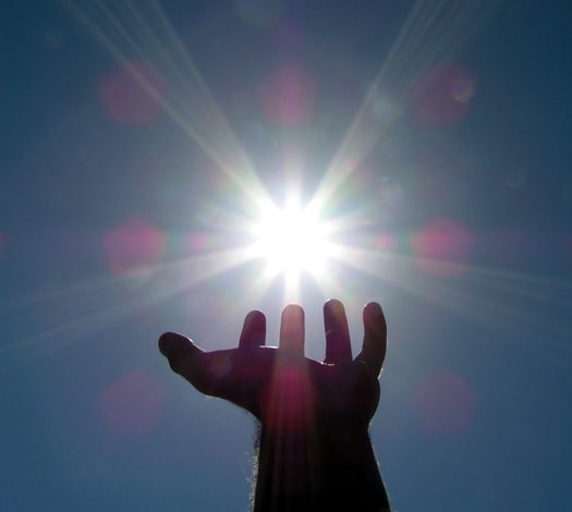 A hand pretends to hold the distant sun in its palm.