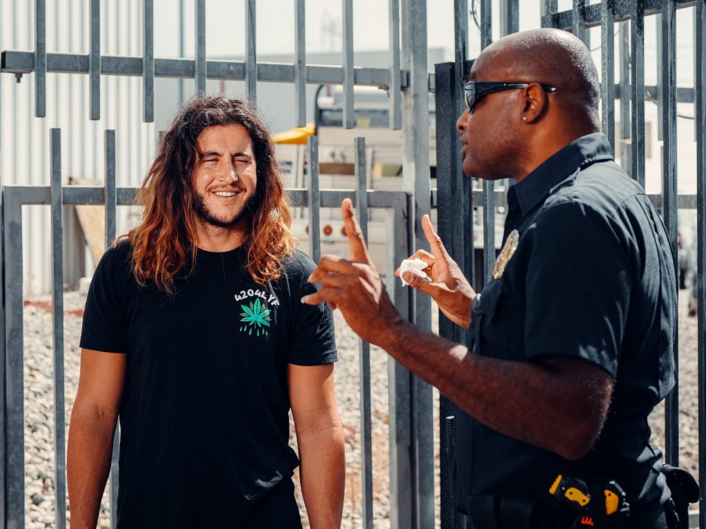 A police officer talking to a man wearing a 420 shirt.