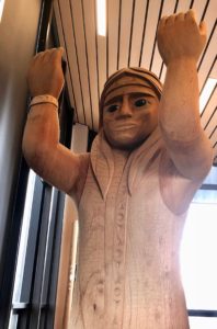 Welcome pole - wooden carving of woman with arms held up and open