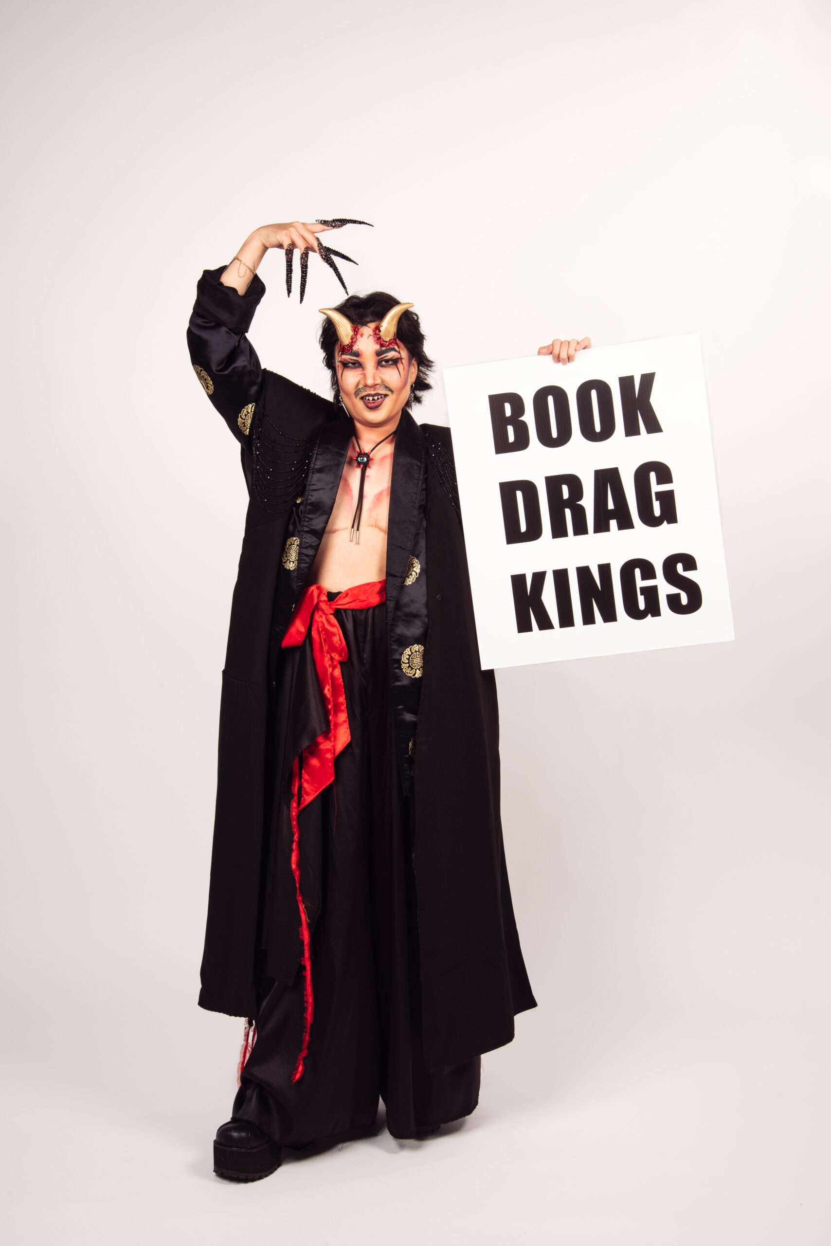 SKIM is wearing a black trench coat and has gold horns on his head with fake blood dripping from them. His chest is bare with contour defining muscles