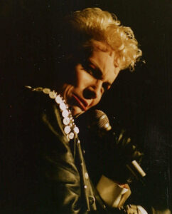 Singer Annie Lennox dressed as Elvis Presley for a performance at the Rock am Ring in 1987. She has short curly hair and is wearing a black leather jacket.