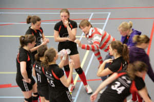 A women's volleyball team on a time out being instructed by their coach.