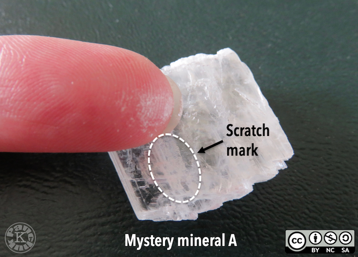 A colourless translucent mineral displays a scratch mark made by a fingernail.