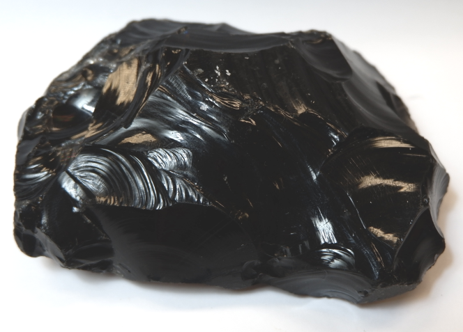 A black rock with a glassy surface. Pieces have been chipped away from the surface, leaving curved breaks behind.