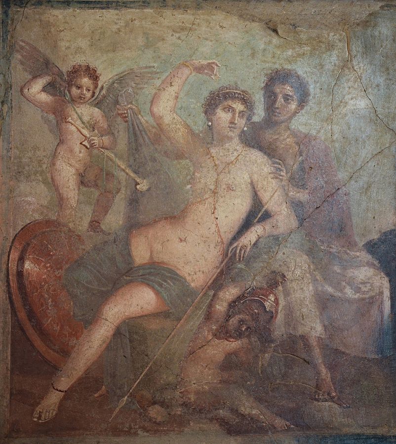 A wall fresco of Venus in partially nude, seated, accompanied by 2 cupids and the god Mars. Mars is undressing Venus, and his bronze shield is propped against the wall behind them.