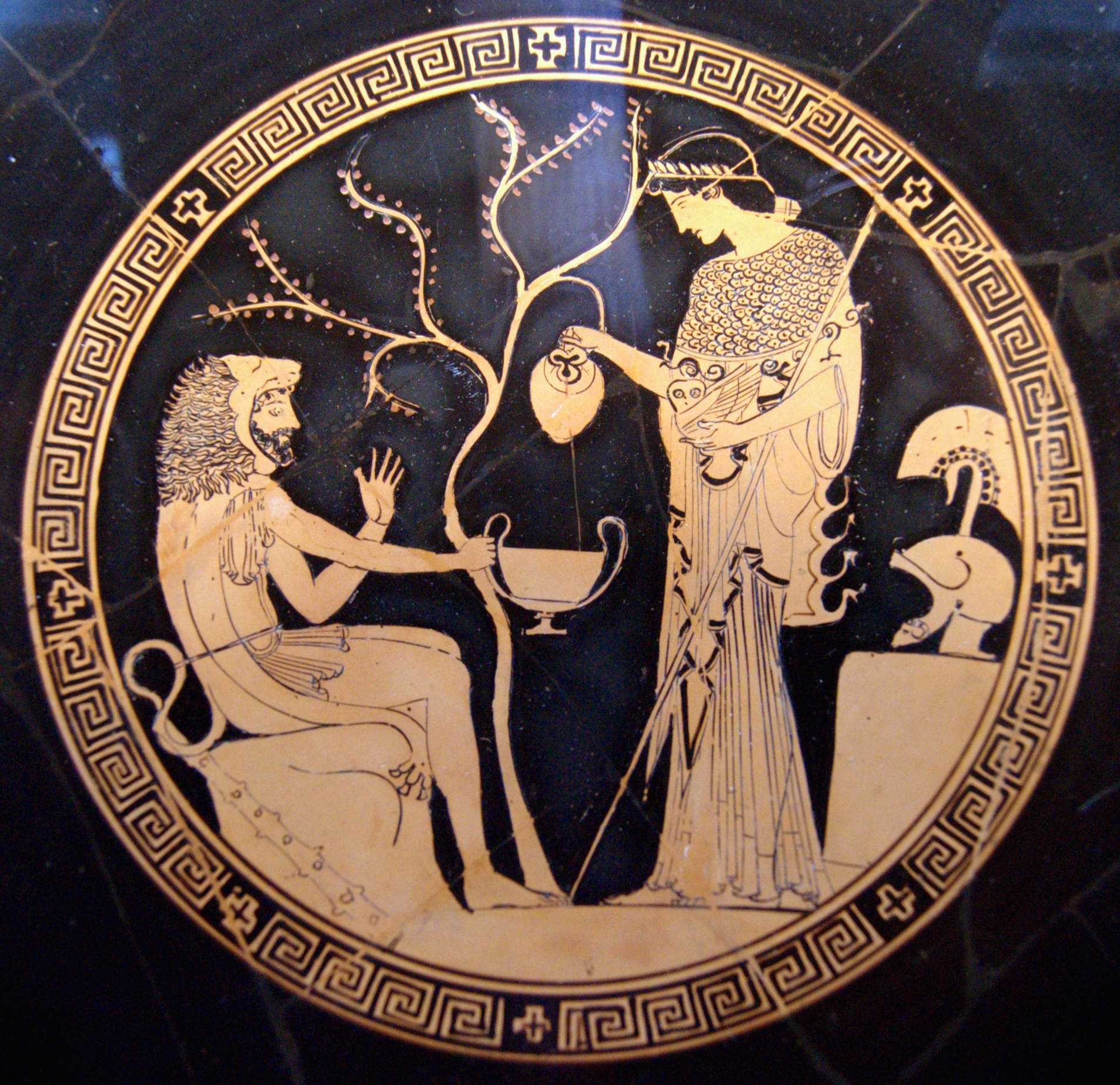 Heracles sits wearing his lion skin and holding a cup. Athena stands before him pouring a liquid into his cup. Athena is wearing the aegis and holding a spear, and her helm rests beside her.