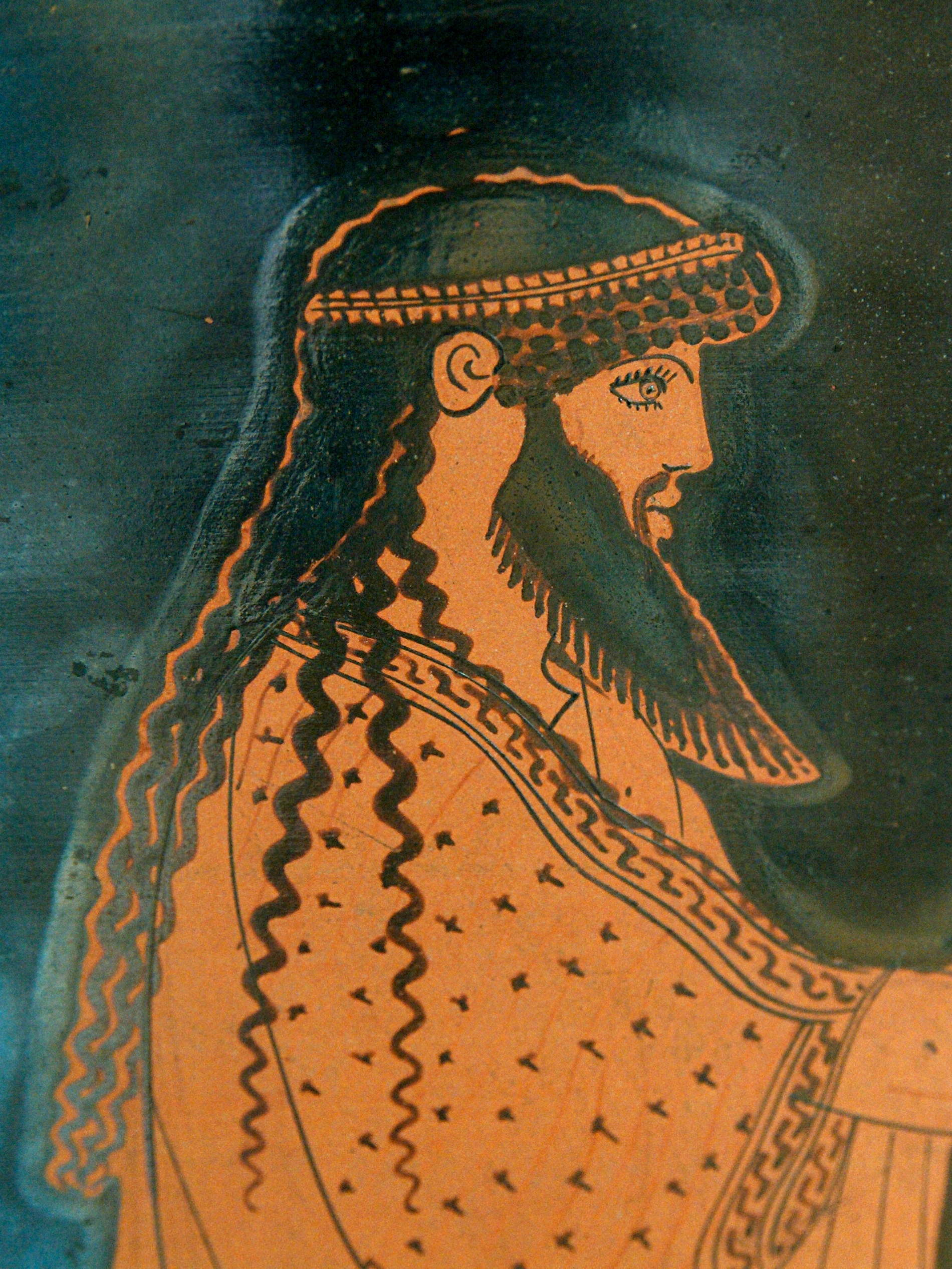 Side view of head and torso of Poseidon. He is bearded with long hair and ornate garments.