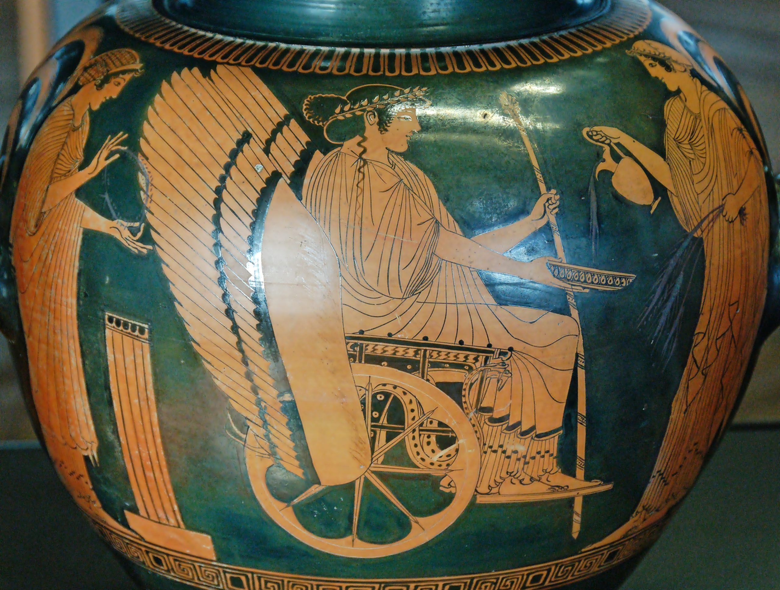 Triptolemos seated in a winged chariot and holding a scepter. Behind him stands Persephone, and in front of him stands Demeter with sheaves of wheat.