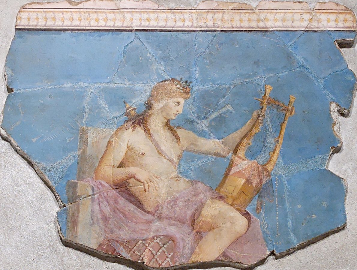 Apollo reclines on a throne in front of a sky-blue background. He holds a lyre and wears a jeweled headdress. He is nude, with a pink cloth draped around his waist.