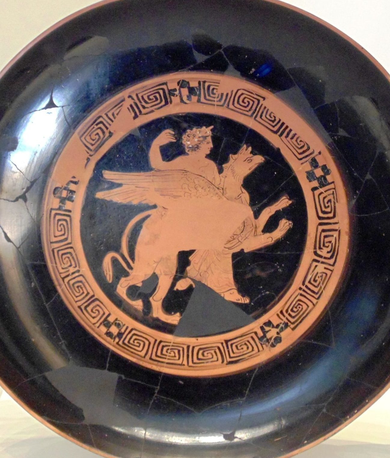 Apollo, wearing a crown of laurels, rides a winged griffin.