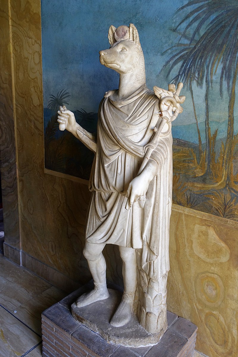 Hermanubis, a person with the head of a jackal. He wears a tunic and chlamys, and carries a winged scepter twined with snakes.