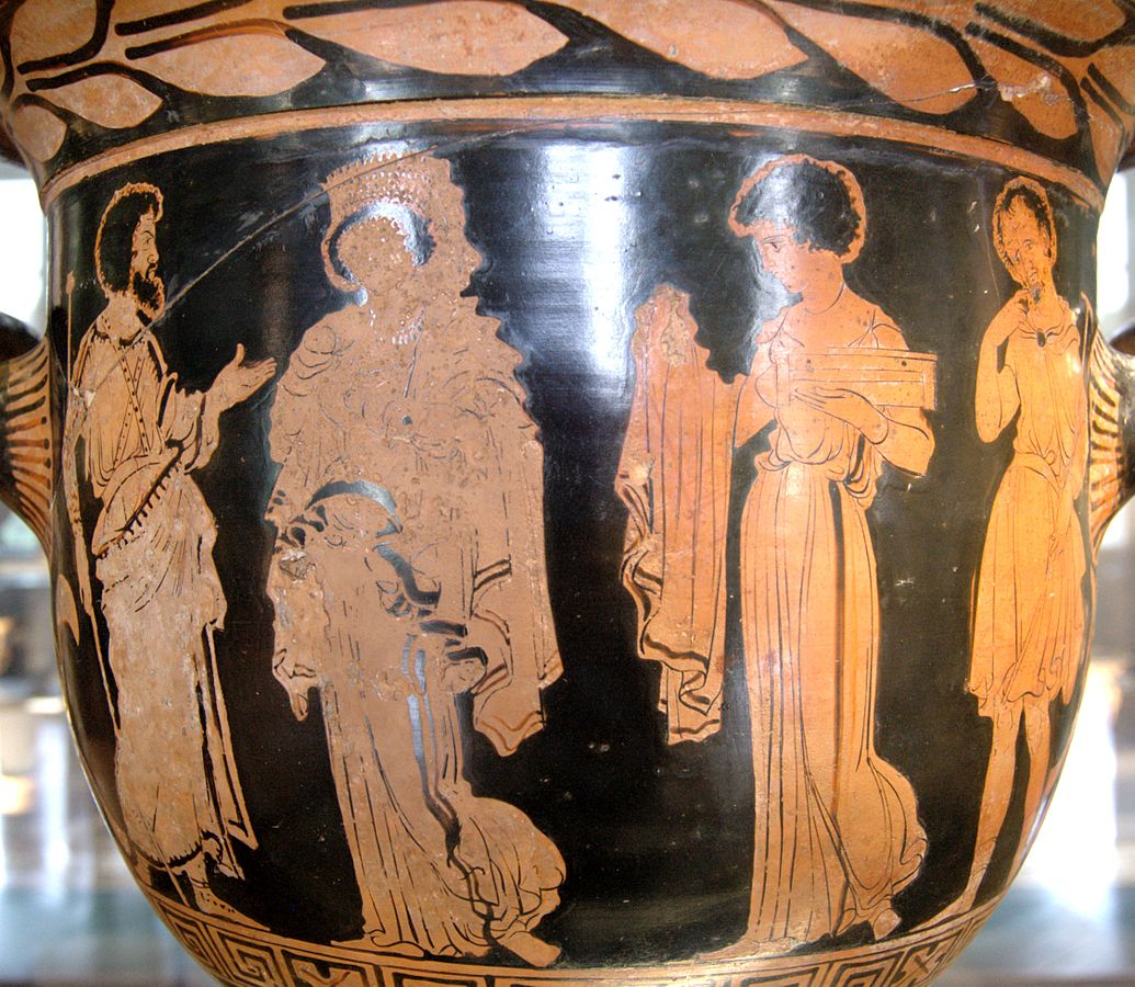 Jason and Creusa, both lavishly dressed, stand side by side. Medea approaches holding a garment draped over her arm and a box to present as gifts.