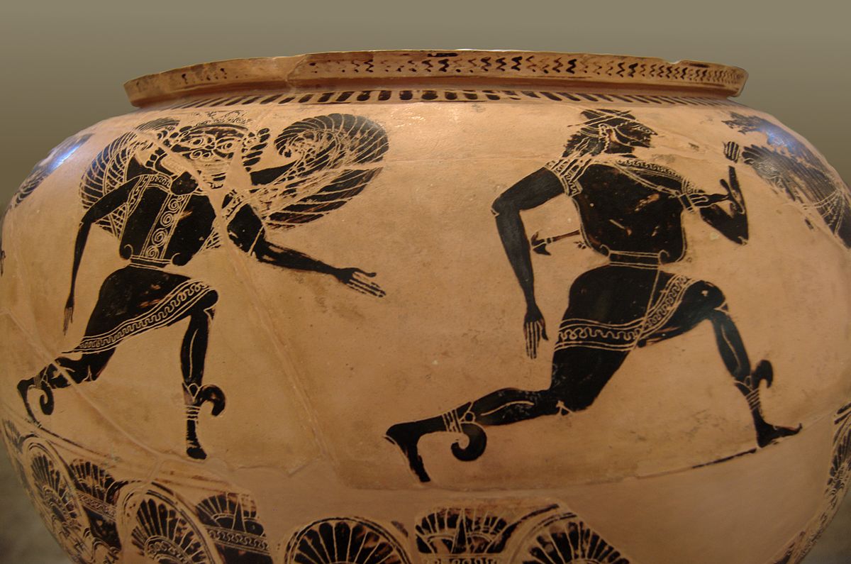 Perseus runs, chased by a gorgon. She is a winged woman with her tongue sticking out. Another gorgon, also chasing, is just visible around the side of the dinos, following behind.