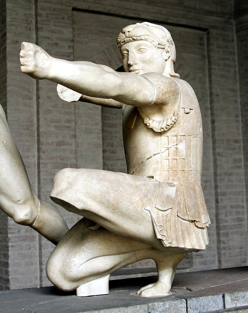 Heracles down on one knee, one arm held out and the other drawn back to shoot a bow (though the bow is missing from the statue. He wears armour and the lion skin cap.