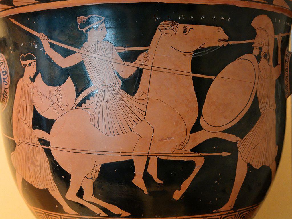 An Amazon, a young woman in a tunic and wielding a spear, rides a horse. She fights a Greek, with a shield and helm, and another Amazons stands behind her.