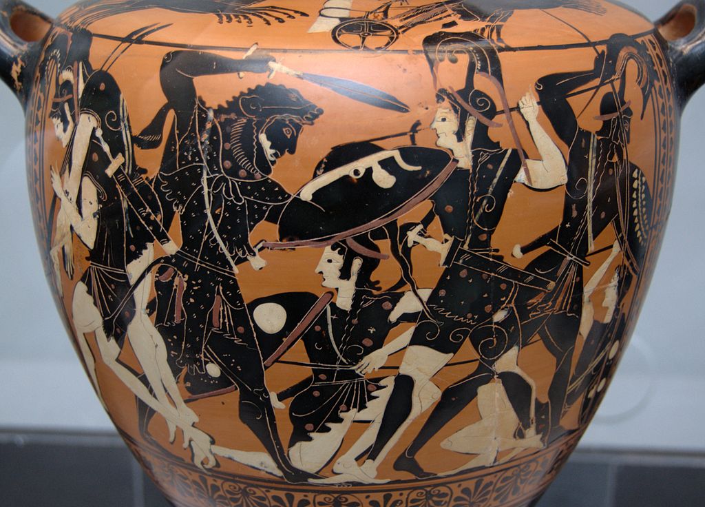 Heracles, wearing his lion skin, lunges at an Amazon with his sword. 5 amazons, and one other Greek warrior, fight around him. One of the Amazons drags a wounded Amazon off the field. The Amazons fight with round shields, helms, and spears.