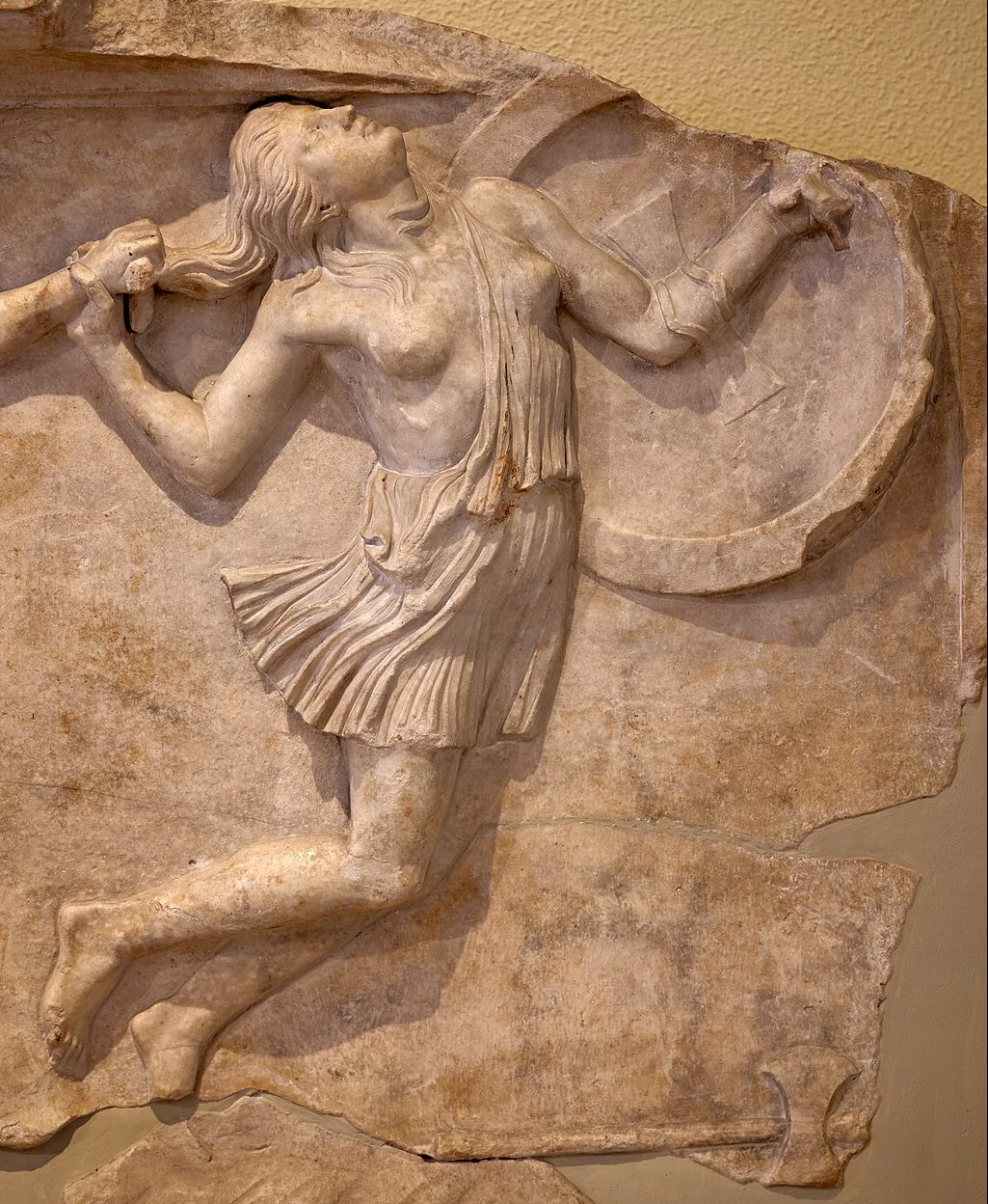 An Amazon, holding a shield an wearing a tunic that leaves one breast bare, stumbles forward, falling as if hit from behind.