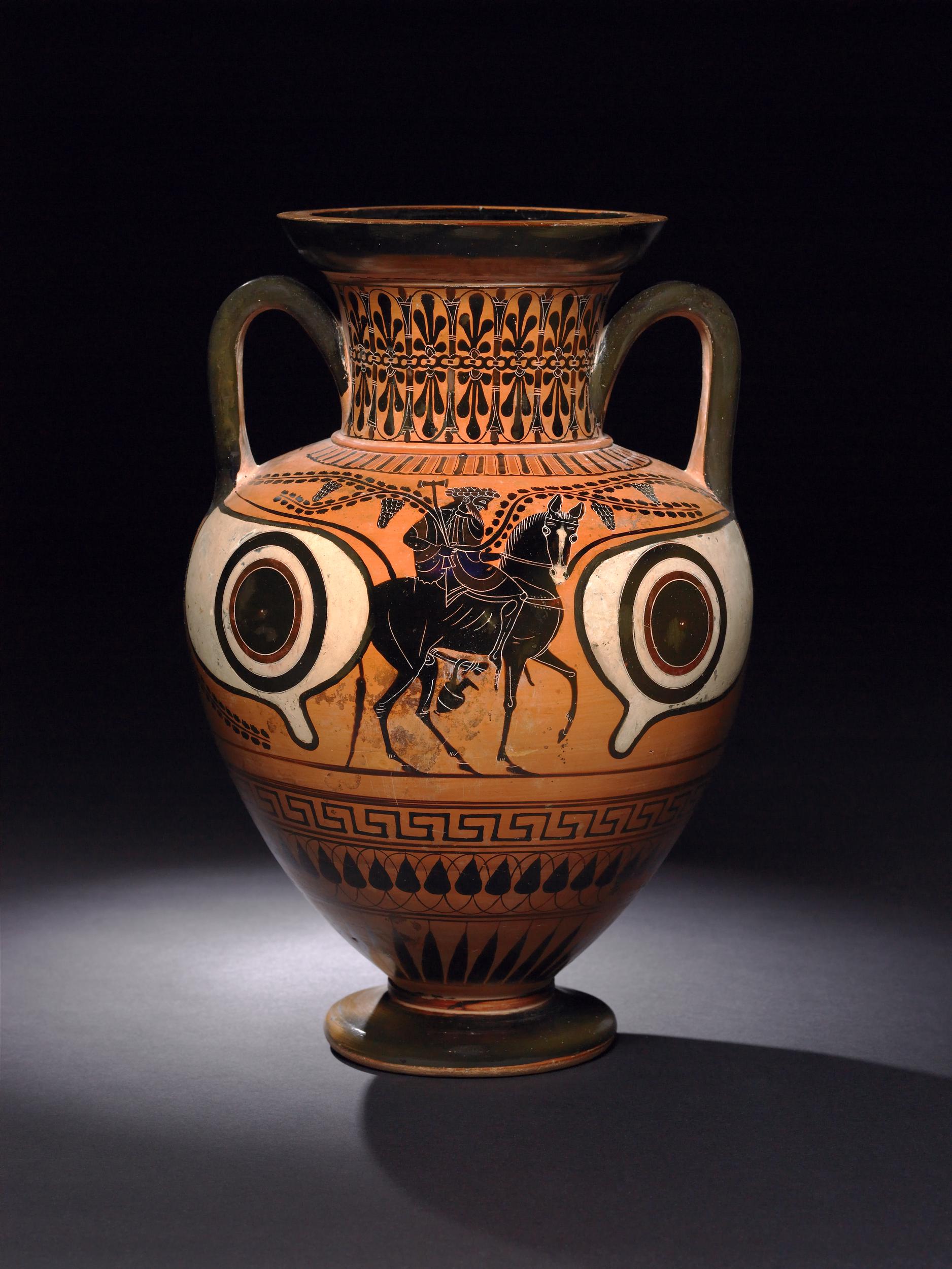 Hephaestus, bearded, crowned, and holding a hammer, rides a mule. Grapevines and a large pair of eyes surround Hephaestus.