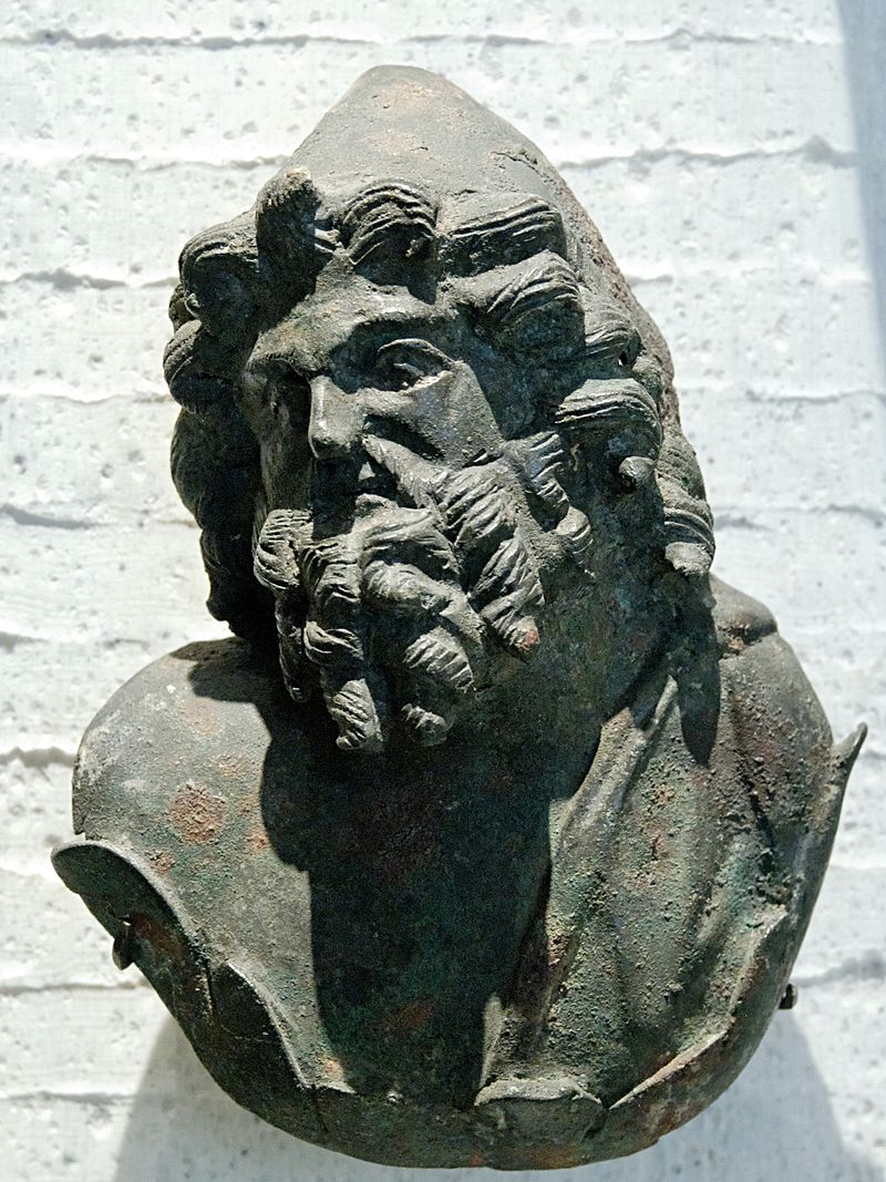 Head and shoulders of Vulcan, bearded with curly hair and wearing a conical pilos hat.