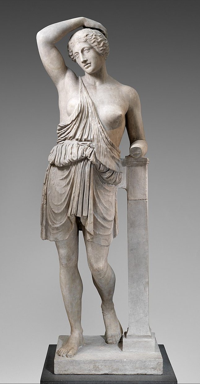 An Amazon, a young woman with a tunic that exposes her left breast and part of her right. She stands with one hand up behind her head, and the other leaning on a plinth.