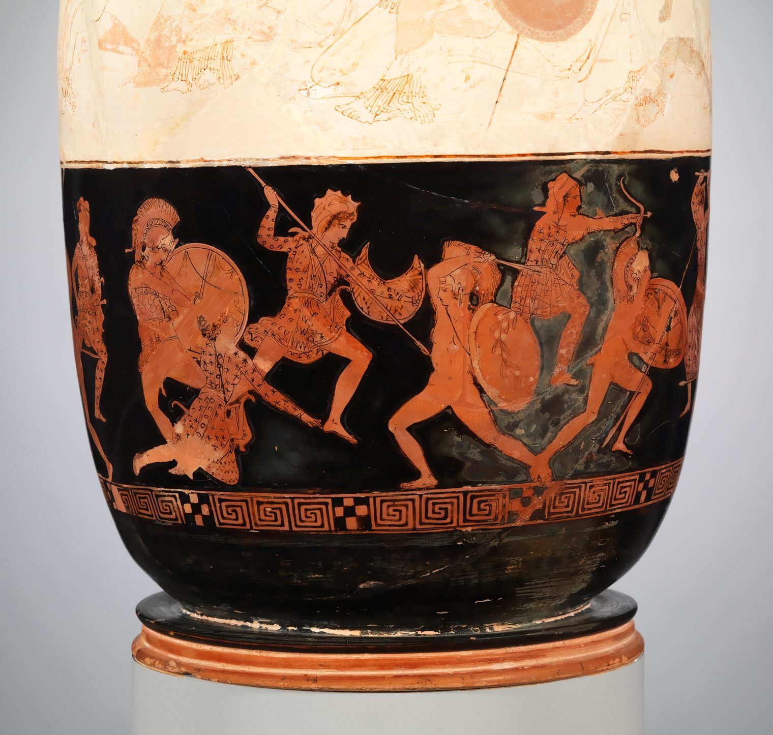 Three Greeks, with helms, swords, and round shields, fight four amazons. The amazons have spears, bows, and crescent-shaped shields. The Amazons wear floppy hats, and wear spotted patterned clothes.