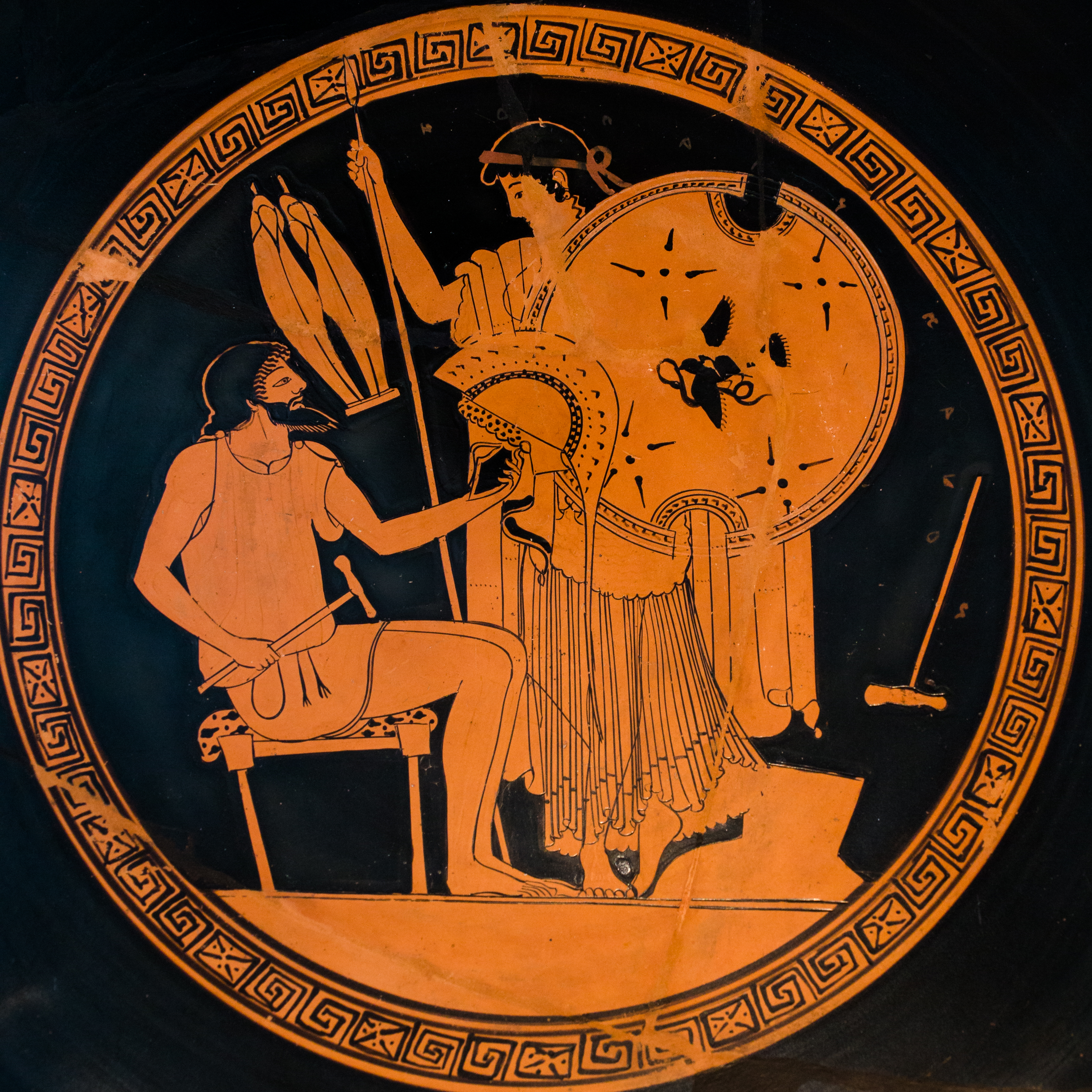Hephaestus, bearded, seated, and holding a hammer, hands a helm to Thetis. Thetis holds a spear and shield.