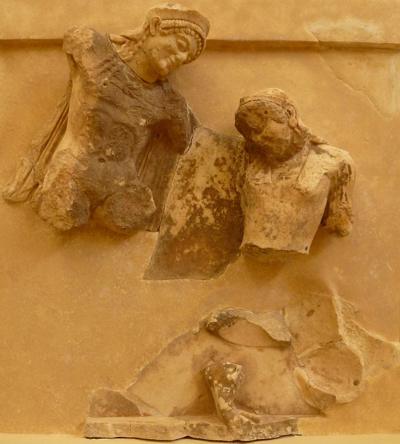 Theseus, with a chlamys cape, crown, and long hair, stands over Antiope, who wears armor. Both reliefs are heavily damaged.