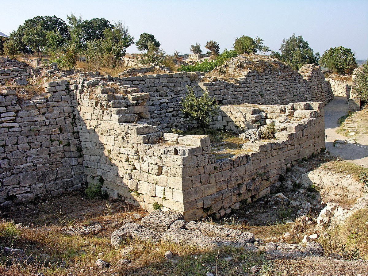 Stone wall remains lining a road or pathway and demarcating a building or chamber..