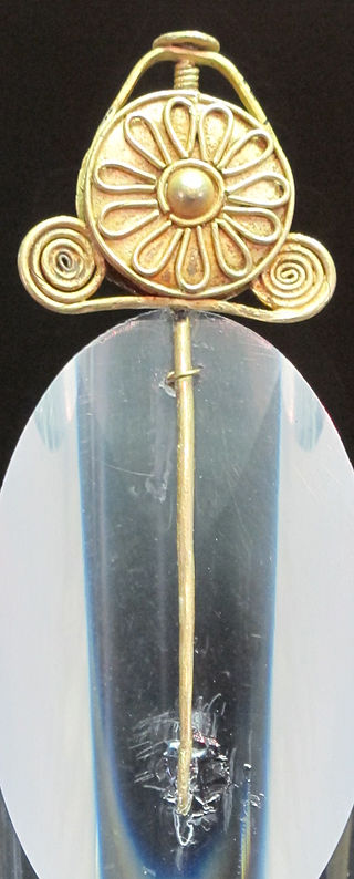 A circular gold brooch with spirals on either side, and a daisy-like pattern in the centre.