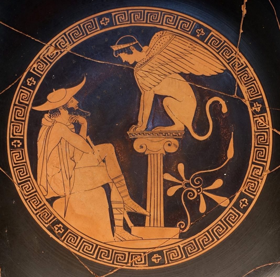 Oedipus, bearded with a petasos hat and chlamys cape, sits on a rock. In front of him, on a column, sits the sphinx, a winged lion with the head of a crowned human.