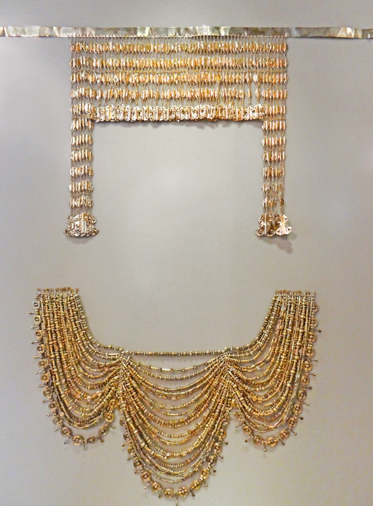 A tasselled gold headdress and a gathered, layered gold necklace.
