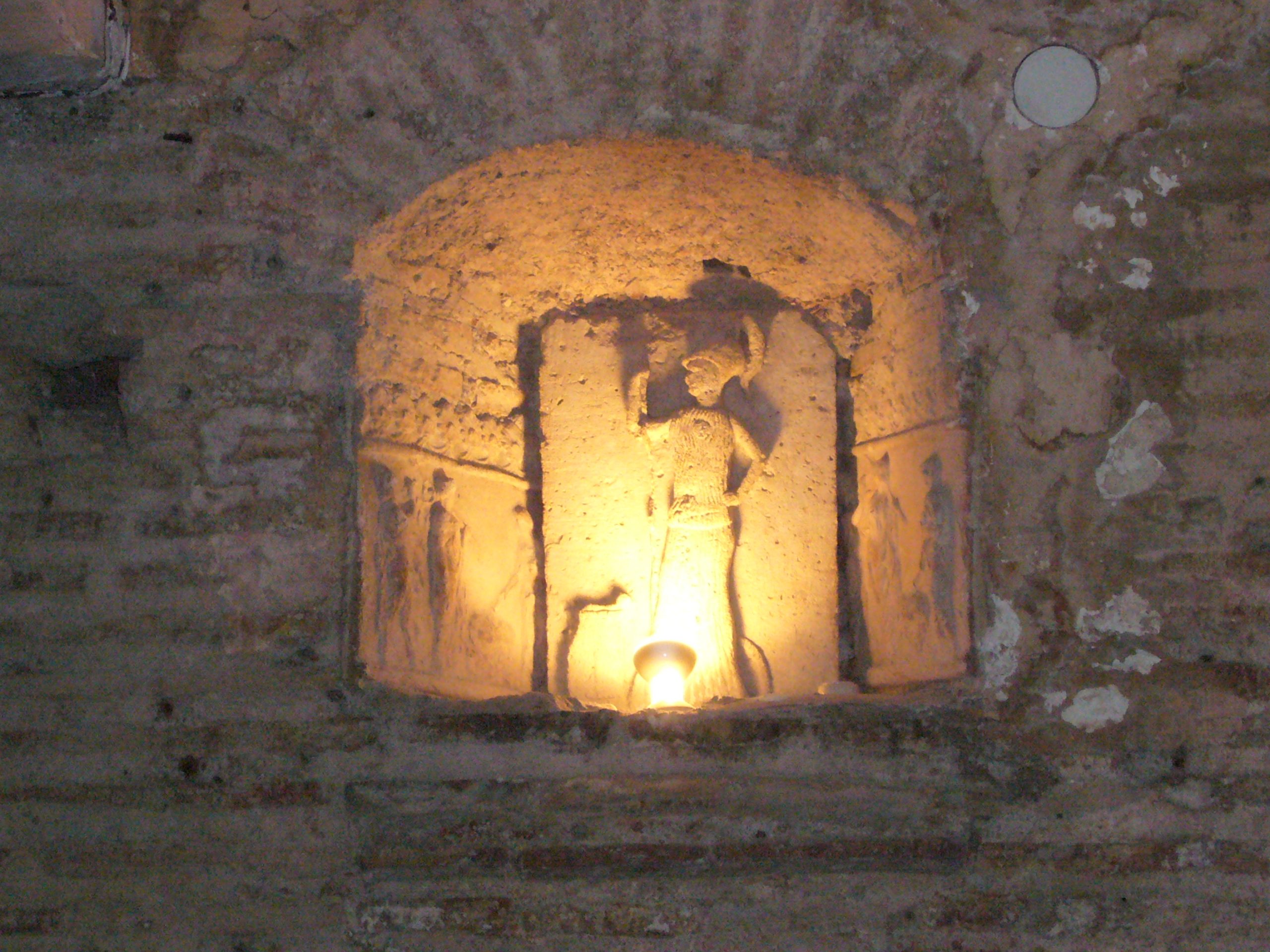 A niche in the wall containing a statuette of a helmed figure, lit from below.
