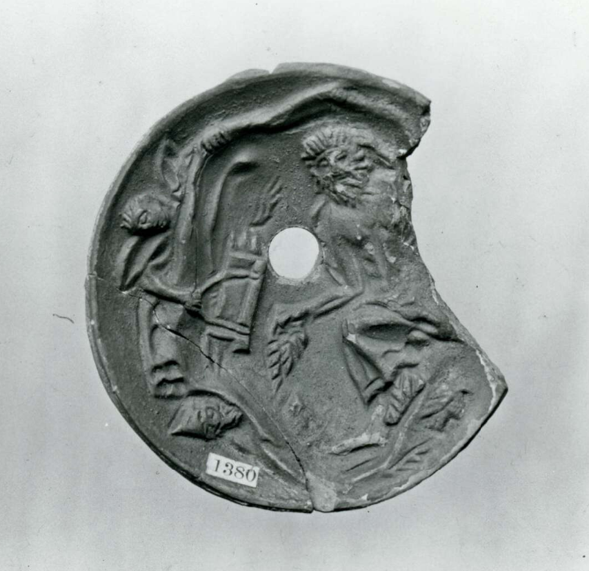 Philoctetes, a bearded man holding a leaf-like wing on one hand, lies in a cave. Odysseus, in a pointed cap, and Neoptolemus, with wings, peer into the cave from the left. A large fragment is missing from the right-hand side of the disk.