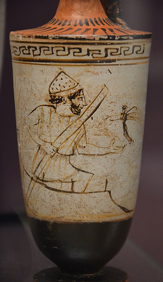 Charon, a bearded man in a tunic and hat, stands on a boat and holds a punting pole. He holds his hand out to a small winged figure of a shade, that flies towards him with its arms extended.