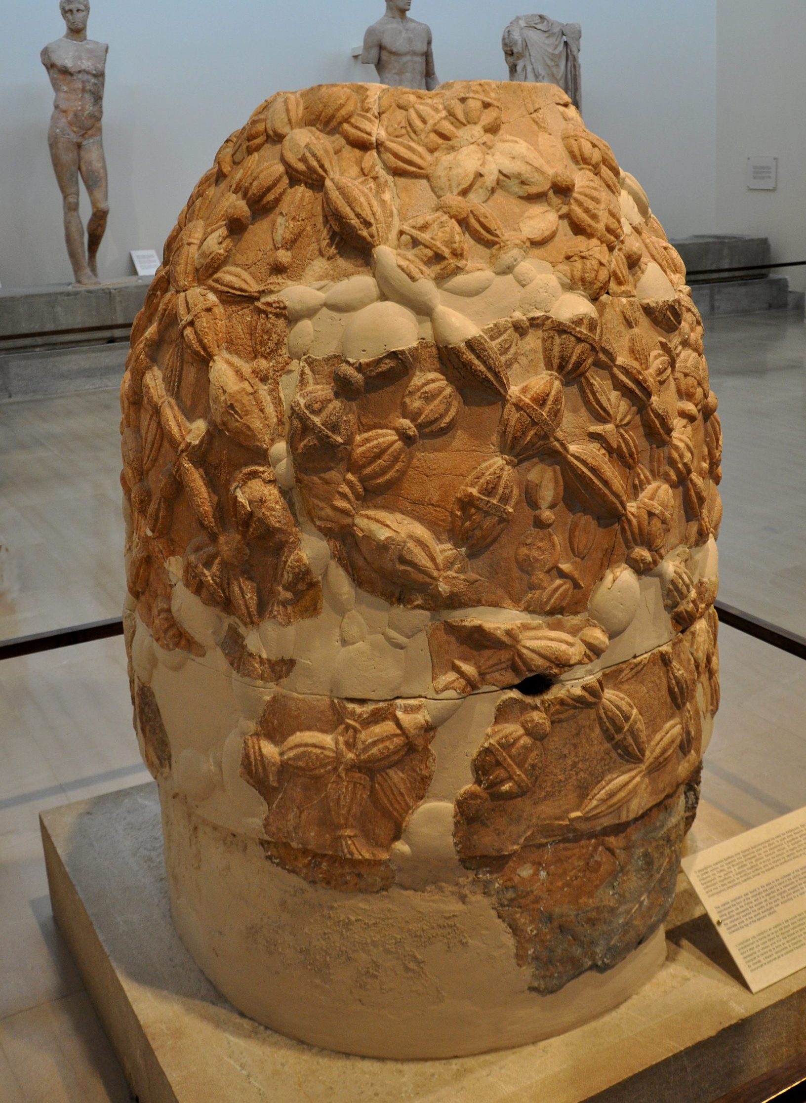 A large, bullet-shaped red terracotta sculpture, embossed with knot-like woven patterns.