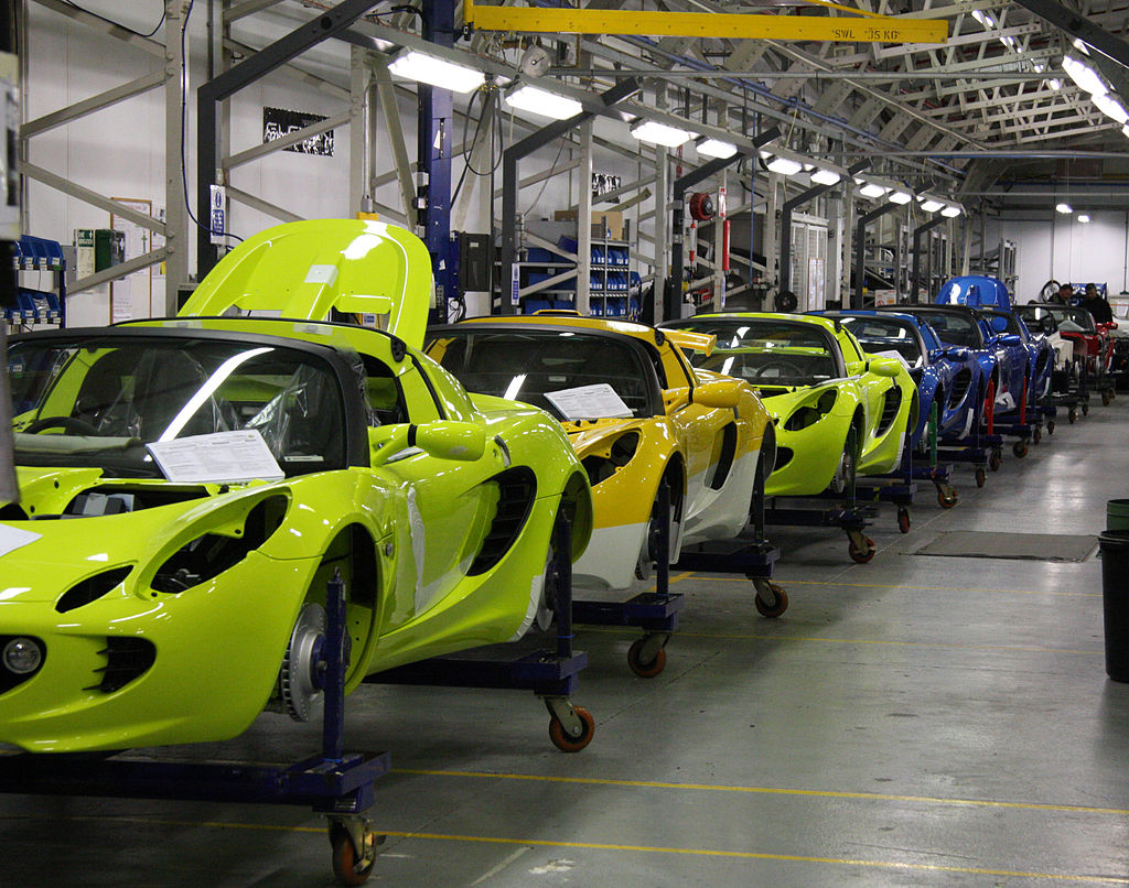 Image shows a long line of sports cars in a factory. The cars are not yet fully assembled.