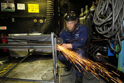 The figure shows a mechanic cutting metal with a metal grinder. The sparks are emerging from the point of contact and jumping off tangentially from the cutter.