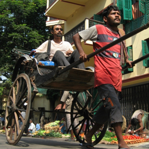 This picture shows a rickshaw driver pulling a passenger down a city street.