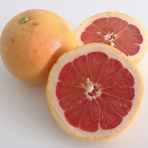 This picture shows two grapefruit, one whole and one cut in half.