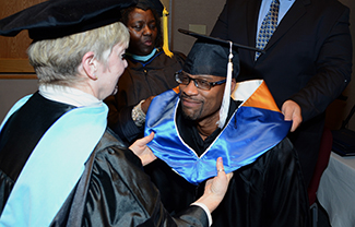 A photograph shows several people are gathered outdoors wearing caps and gowns in a graduation ceremony.